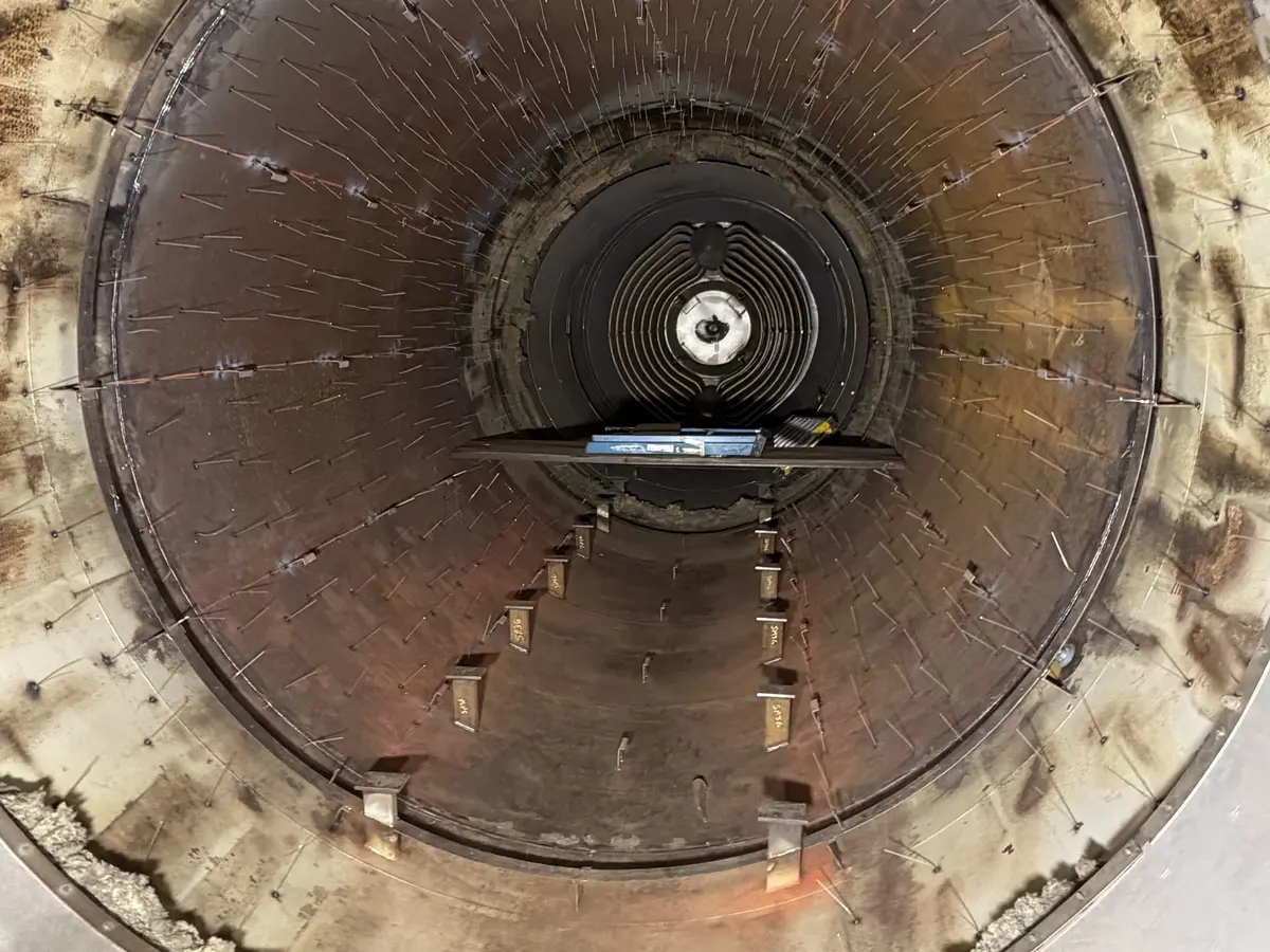 Inside an autoclave shell stripped for re-insulation, weld pins across the barrel and heating elements at the far head.